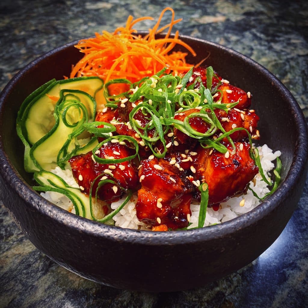A bowl of rice topped with spicy red chicken and fresh vegetables